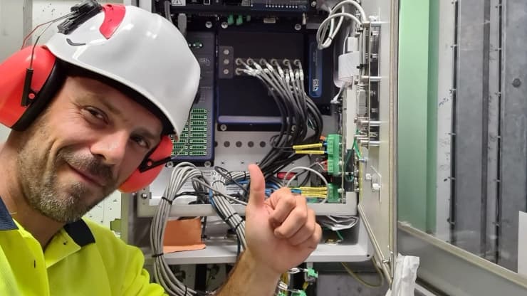 Technician in hard hat giving thumbs up in front of open electrical control cabinet