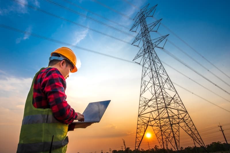 Engineer with a laptop monitoring an electric transmission tower